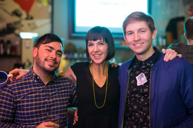 Three attendees smiling at the Love Bomb 2017 event, with drinks in hand, celebrating community support for My Voice Music.